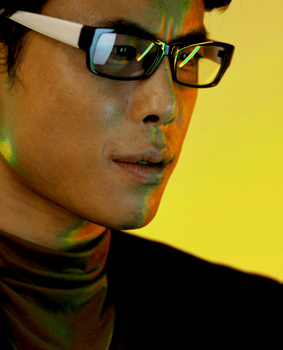 Man in glasses lit by yellow and green light